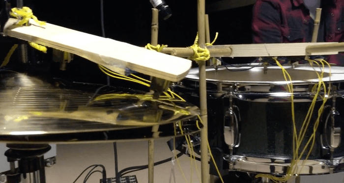 Patchwork's wooden striker arm rigged over a hi-hat cymbal, beside a snare drum